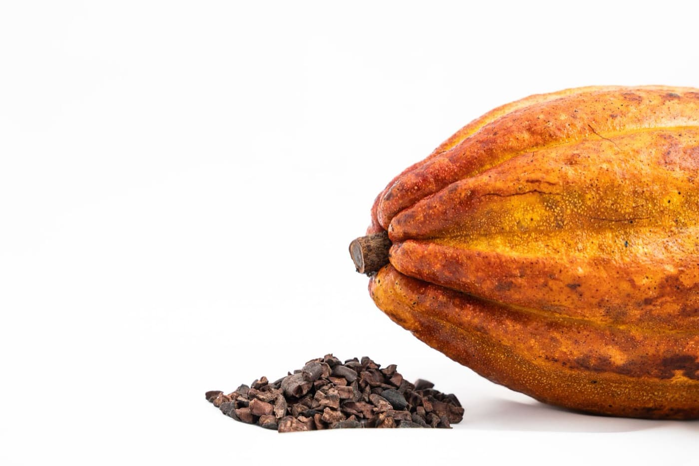 A whole orange cocoa pod beside a small heap of cocoa nibs